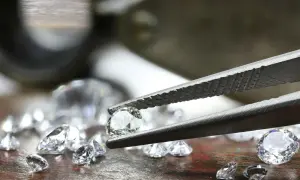 Szczypce trzymają błyszczący diament, obok leżą inne kamienie. To nie jest kaboszon, lecz brylant.