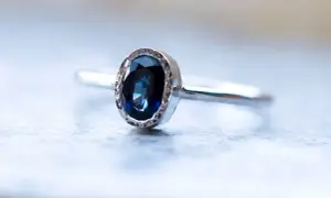 Elegancki pierścionek z owalnym, głęboko niebieskim kamieniem, otoczonym delikatnym, srebrnym wzorem.