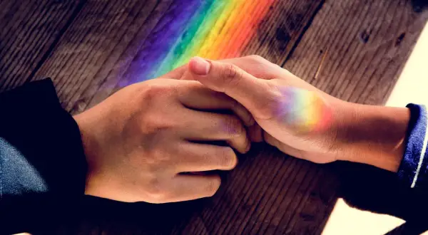 Dłonie splecione na drewnianym blacie, na których widać tęczowe refleksy. To jak pierścionek nastroju znaczenie kolorów, symbolizujący różnorodność i nadzieję.
