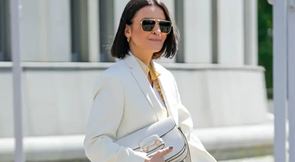 Elegancka kobieta po 50. w białej marynarce i okularach przeciwsłonecznych, z białą torebką. Stylowa moda po 50.