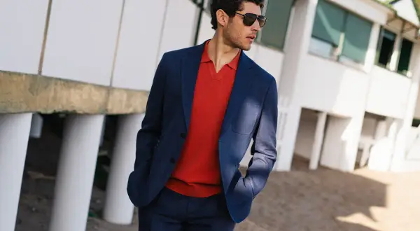 Eleganckie stylizacje na zwiedzanie miasta: mężczyzna w granatowym garniturze i czerwonym polo, z okularami przeciwsłonecznymi, na tle białego budynku.