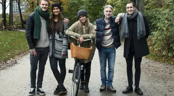 Pięcioro przyjaciół w jesiennych stylizacjach, przykład szwedzkiego stylu ubierania. Jeden z nich ma rower z wiklinowym koszykiem.