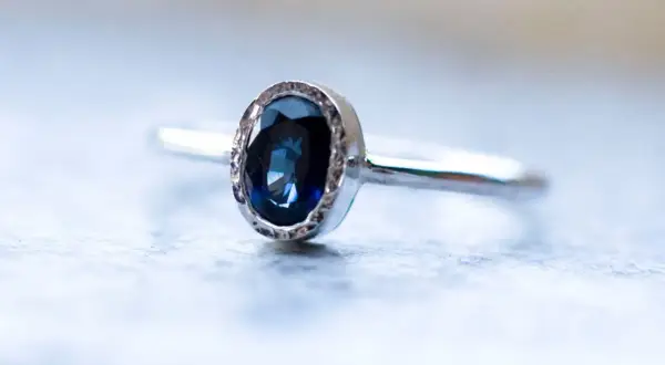 Elegancki pierścionek z owalnym, głęboko niebieskim kamieniem, otoczonym delikatnym, srebrnym wzorem.
