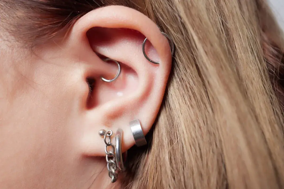 Ucho z kilkoma kolczykami, w tym daith piercing, helix i ozdobne kółka z łańcuszkiem.