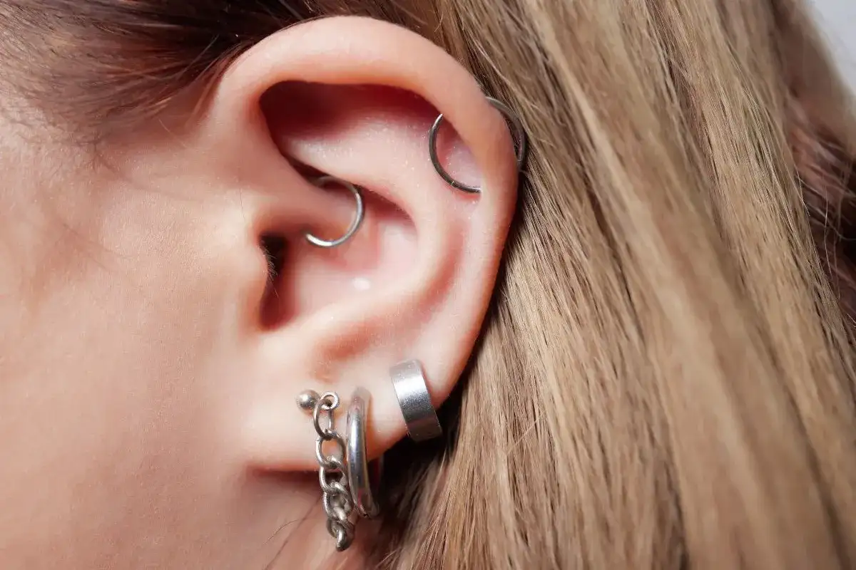 Ucho z kilkoma kolczykami, w tym daith piercing, helix i ozdobne kółka z łańcuszkiem.
