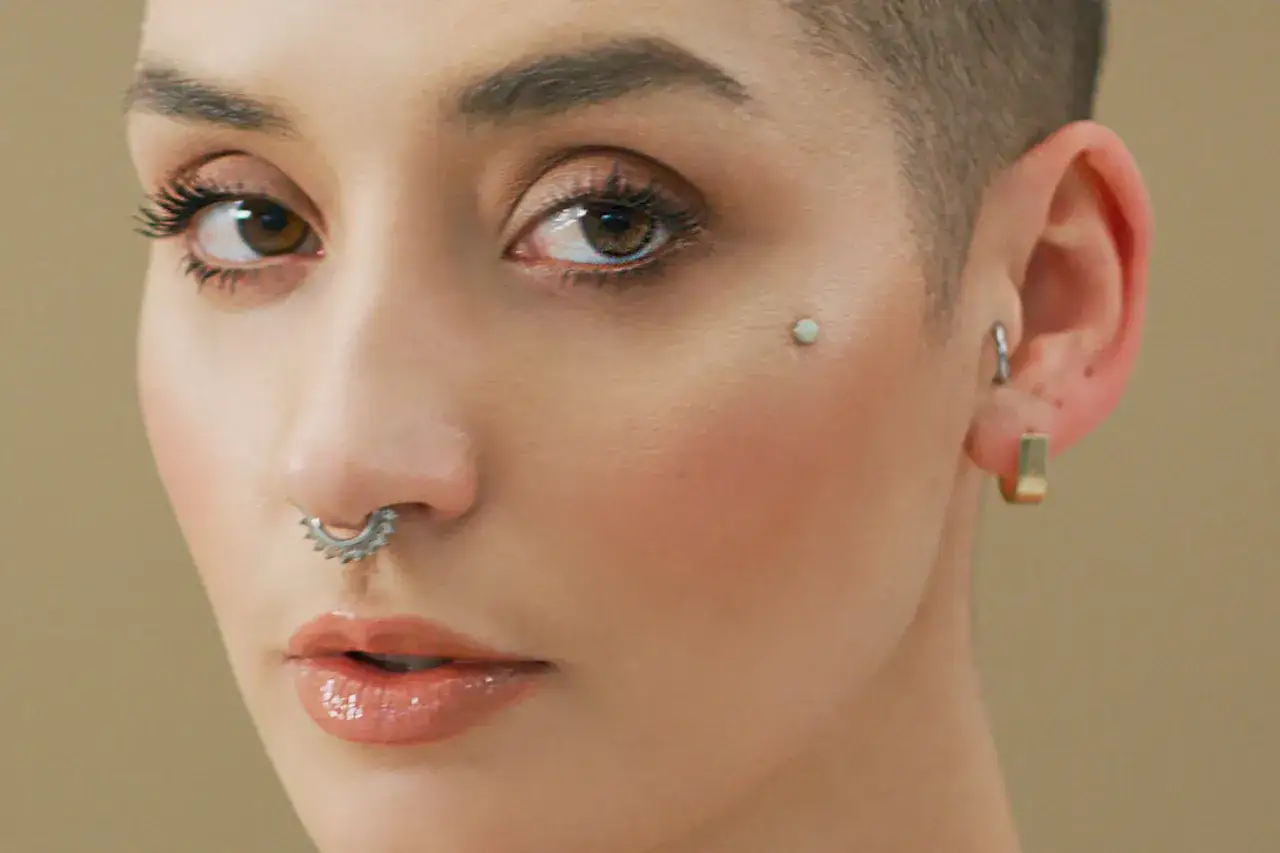 Delikatny kolczyk pod skórą na policzku, ozdobiony septum i kolczykami w uszach, podkreśla urodę kobiety.