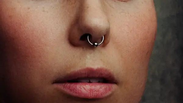 Zbliżenie na twarz z piegami i kolczykiem w nosie. Ile goi się septum? To pytanie zadaje sobie wiele osób decydujących się na ten rodzaj piercingu.
