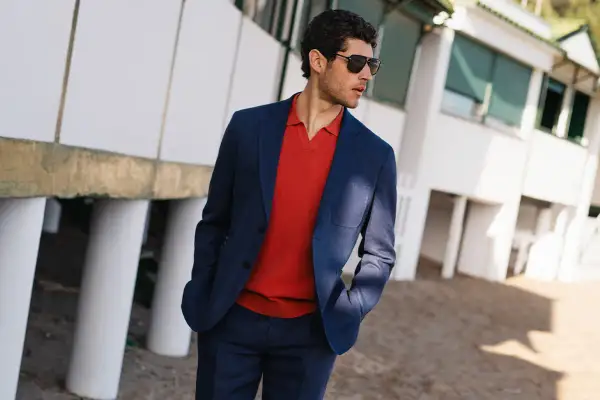 Eleganckie stylizacje na zwiedzanie miasta: mężczyzna w granatowym garniturze i czerwonym polo, z okularami przeciwsłonecznymi, na tle białego budynku.