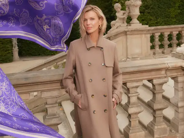 Elegancka kobieta w beżowym płaszczu, obok niej powiewa fioletowy szal z wzorem. Zastanawiasz się, jaki kolor pasuje do fioletu? Beż jest doskonałym wyborem!