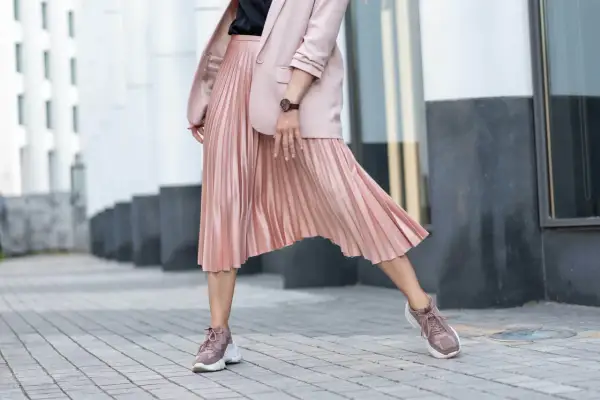 Jakie buty do plisowanej spódnicy? Sneakersy w pudrowym różu świetnie komponują się z satynową spódnicą i marynarką, tworząc modny look.